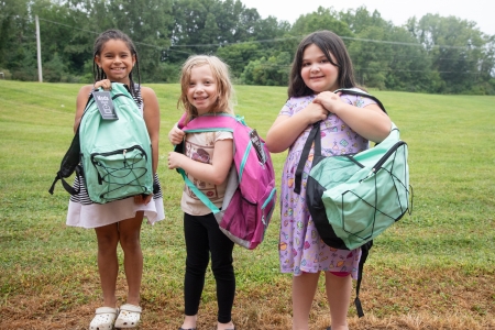 Three young girls showing off their new backpacks by holding them in front of them.