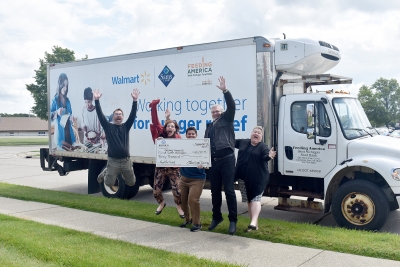 Five people jumping for joy while holding a physically large check in front of a box truck.