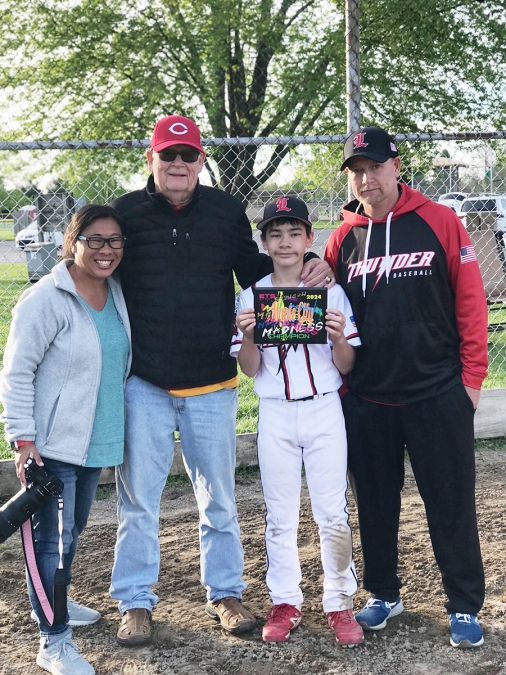 A group photo including a woman holding a camera and a young boy in baseball uniform.