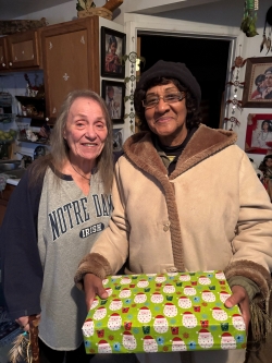 Two women standing side-by-side, one holding a christmas present. 