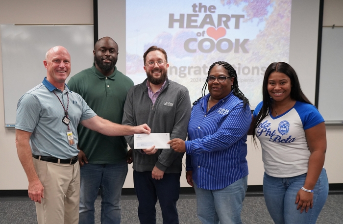 5 people standing to0gether, smiling at the camera while holding a check.