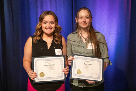 Two young women standing next to each other, both holding certificates. 