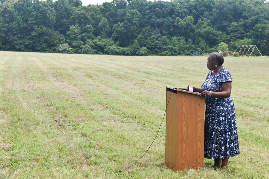 A woman stands at a podium with an expansive, vacant field behind her. 